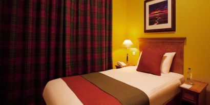 Single bed guest room in The Royal Highland Hotel, with bedside lamp and art on the wall.