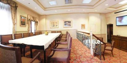 Hotel meeting room, with long table, surrounding chairs, and a large TV on the wall.