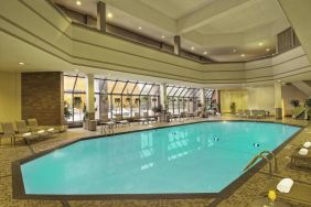 The indoor pool has nearby chairs, tables, and loungers, plus large windows.