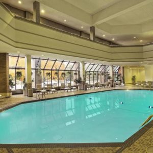 The indoor pool has nearby chairs, tables, and loungers, plus large windows.