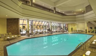 The indoor pool has nearby chairs, tables, and loungers, plus large windows.