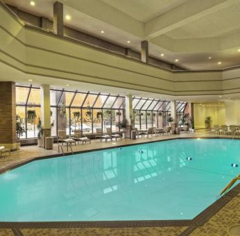 The indoor pool has nearby chairs, tables, and loungers, plus large windows.