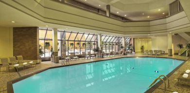 The indoor pool has nearby chairs, tables, and loungers, plus large windows.