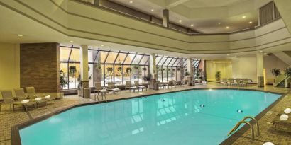 The indoor pool has nearby chairs, tables, and loungers, plus large windows.