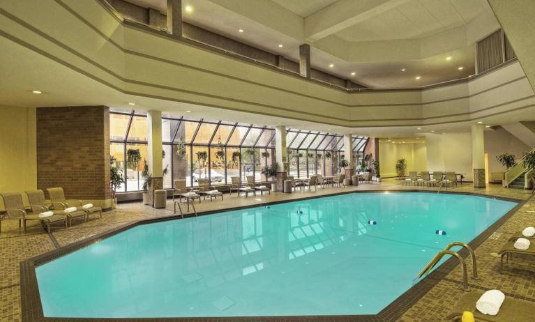 The indoor pool has nearby chairs, tables, and loungers, plus large windows.