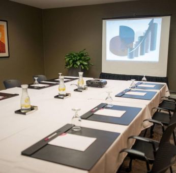 Executive meeting room with long table, surrounding chairs, and a projector screen.