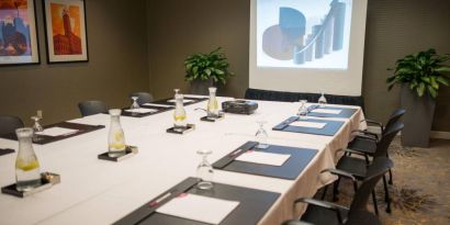 Executive meeting room with long table, surrounding chairs, and a projector screen.