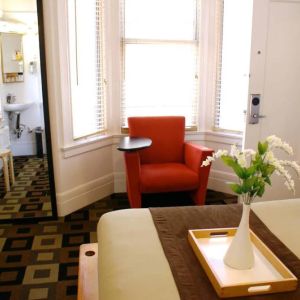 Guest room of The Mosser Hotel, with bed, chair, windows, and ensuite bathroom.