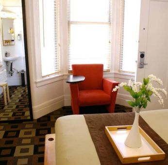 Guest room of The Mosser Hotel, with bed, chair, windows, and ensuite bathroom.