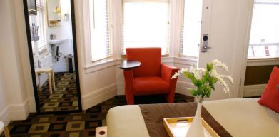 Guest room of The Mosser Hotel, with bed, chair, windows, and ensuite bathroom.