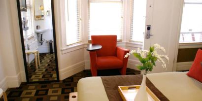 Guest room of The Mosser Hotel, with bed, chair, windows, and ensuite bathroom.