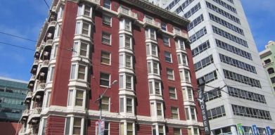 Exterior of the Mosser Hotel, with vertical sign and vibrant red brick hue.