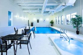 The hotel’s indoor swimming pool has tables, chairs, potted plants, and a hot tub nearby.