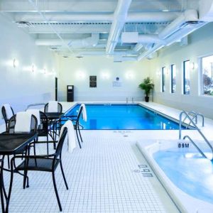 The hotel’s indoor swimming pool has tables, chairs, potted plants, and a hot tub nearby.