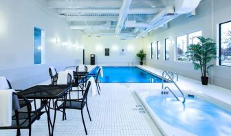 The hotel’s indoor swimming pool has tables, chairs, potted plants, and a hot tub nearby.