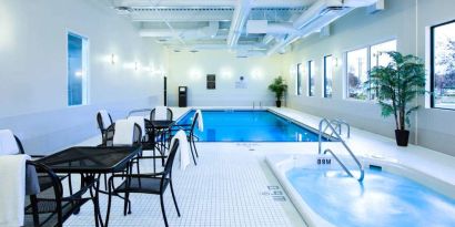 The hotel’s indoor swimming pool has tables, chairs, potted plants, and a hot tub nearby.