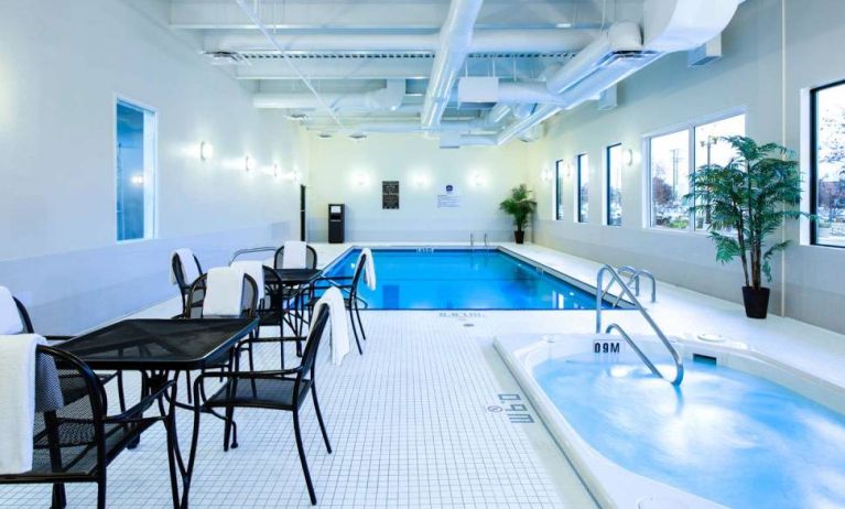 The hotel’s indoor swimming pool has tables, chairs, potted plants, and a hot tub nearby.