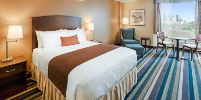 Double bed guest room in Best Western Plus Winnipeg Airport, featuring window, armchair, and foot stool.