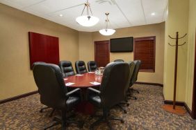 Hotel meeting room with long wooden table, plush leather swivel chairs, and widescreen TV.