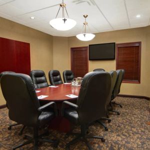 Hotel meeting room with long wooden table, plush leather swivel chairs, and widescreen TV.