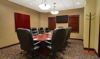 Hotel meeting room with long wooden table, plush leather swivel chairs, and widescreen TV.