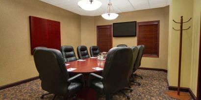 Hotel meeting room with long wooden table, plush leather swivel chairs, and widescreen TV.