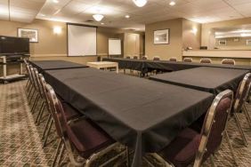 Meeting room in Quality Inn Hotel Medicine Hat, with tables arranged in a U-shape, surrounding chairs, large TV, and projector screen.