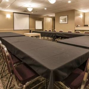 Meeting room in Quality Inn Hotel Medicine Hat, with tables arranged in a U-shape, surrounding chairs, large TV, and projector screen.