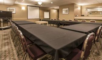 Meeting room in Quality Inn Hotel Medicine Hat, with tables arranged in a U-shape, surrounding chairs, large TV, and projector screen.