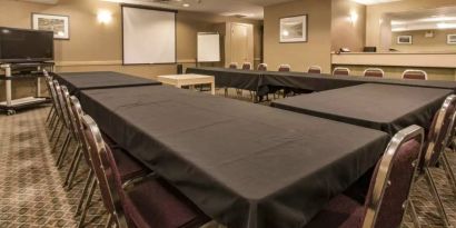 Meeting room in Quality Inn Hotel Medicine Hat, with tables arranged in a U-shape, surrounding chairs, large TV, and projector screen.