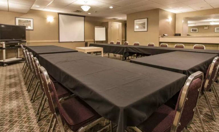 Meeting room in Quality Inn Hotel Medicine Hat, with tables arranged in a U-shape, surrounding chairs, large TV, and projector screen.