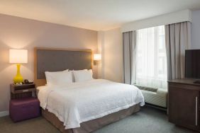 One of the Hampton Inn Times Square South’s king bed guest rooms, with window, TV, and bedside table.