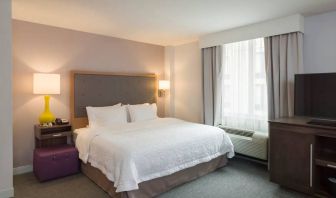 One of the Hampton Inn Times Square South’s king bed guest rooms, with window, TV, and bedside table.