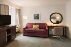 The Hampton Inn Times Square South’s king mobility suite lounge, with desk, sofa, and television.