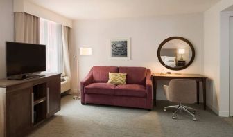 The Hampton Inn Times Square South’s king mobility suite lounge, with desk, sofa, and television.