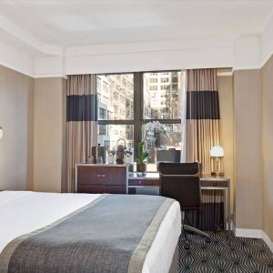 Guest room in the New Yorker Hotel, A Wyndham Hotel, with double bed and workspace desk and chair.