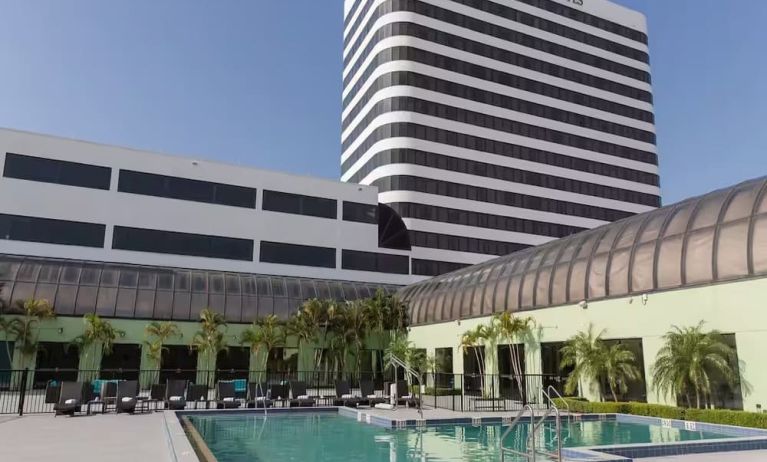 Pool area with seating area and sun beds at Embassy Suites By Hilton West Palm Beach Central.