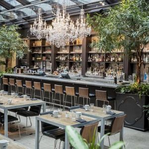 The hotel’s restaurant and bar, with table seating, tall barstools, and plenty of plant life.