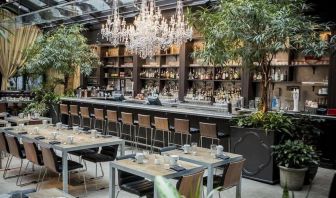 The hotel’s restaurant and bar, with table seating, tall barstools, and plenty of plant life.