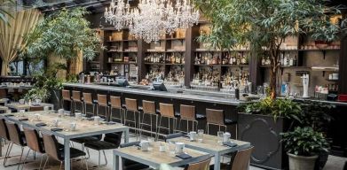 The hotel’s restaurant and bar, with table seating, tall barstools, and plenty of plant life.