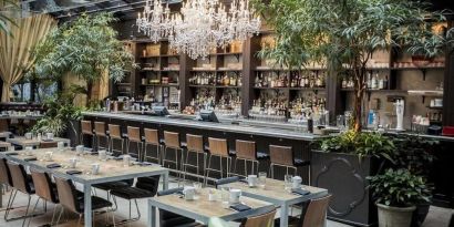 The hotel’s restaurant and bar, with table seating, tall barstools, and plenty of plant life.