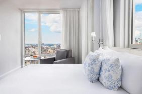 One of the NoMo Soho’s guest rooms, with double bed, chair, and great view of the city.