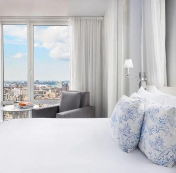 One of the NoMo Soho’s guest rooms, with double bed, chair, and great view of the city.