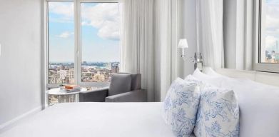 One of the NoMo Soho’s guest rooms, with double bed, chair, and great view of the city.