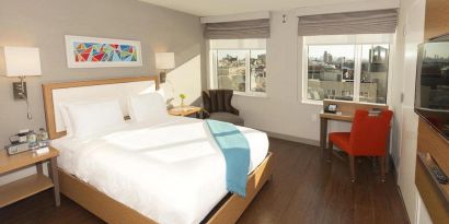 Guest room in Edge Hotel NYC, with two windows, double bed, and workspace desk and chair.