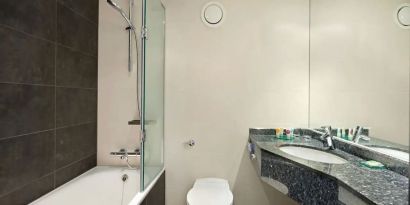 Private guest bathroom with shower and bath at Hyatt Place London Heathrow Airport.