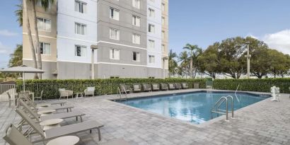 Loungers beside outdoor pool at Homewood Suites By Hilton Miami Airport-Blue Lagoon.