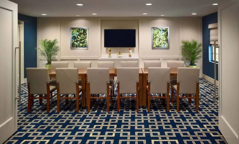 Meeting room in Sonesta ES Suites Tucson, featuring long wooden table, seating for twelve, and a large, wall-mounted television.