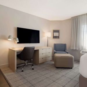 Guest room workspace in Sonesta Simply Suites Irvine East Foothill, furnished with desk, chair, lamp, and television.