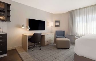 Guest room workspace in Sonesta Simply Suites Irvine East Foothill, furnished with desk, chair, lamp, and television.